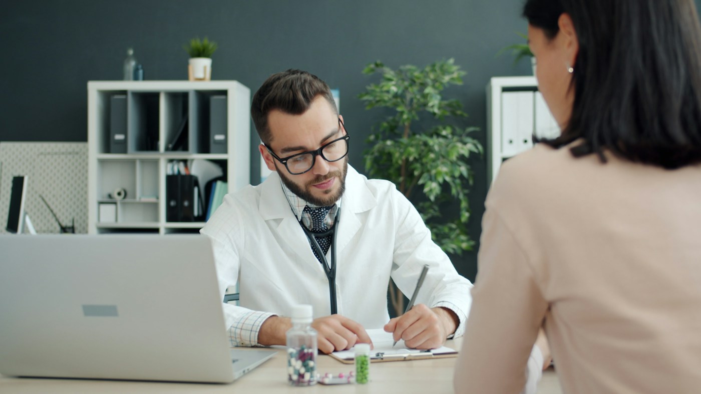 Illustrative younger healthcare professional consulting with an adult at a desk; stock models are not presented as IMULIFE staff or patients.